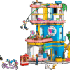 A brightly lit showroom display featuring a completed Friends Clubhouse LEGO set showcasing its tan walls pink roofs and mini dolls playing in the yard