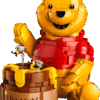 LEGO Winnie Pooh storybook display model featuring Pooh's brick built oak tree house with green foliage and beehives surrounded by character minifigures like Piglet and Eeyore